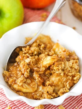 A serving of apple crisp in a bowl with a metal spoon on top of a striped placemat