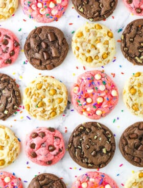 Four different kinds of cake mix cookies lined up on a marble countertop including flavors like chocolate, strawberry and butterscotch