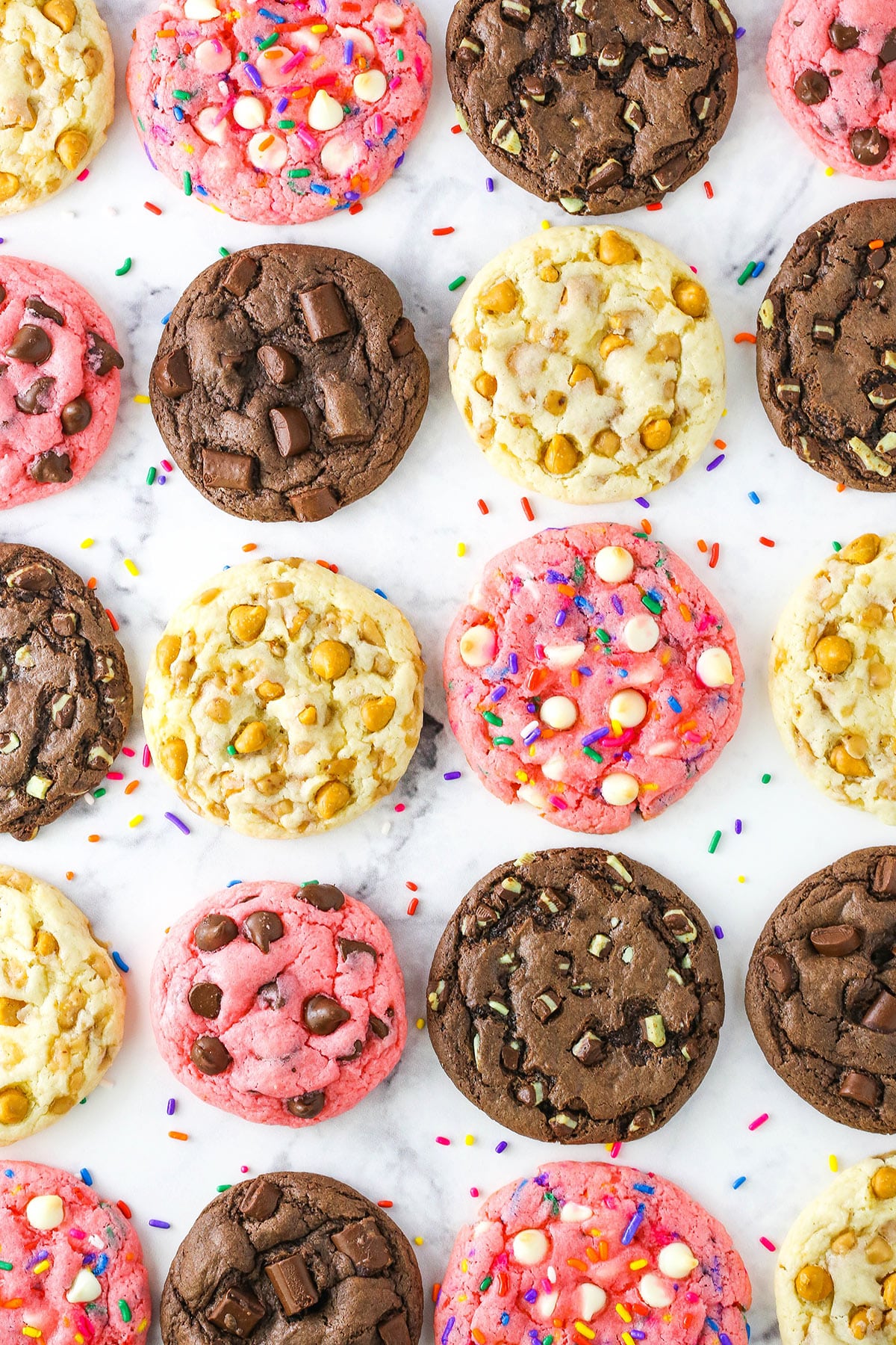 Four different kinds of cake mix cookies lined up on a marble countertop including flavors like chocolate, strawberry and butterscotch