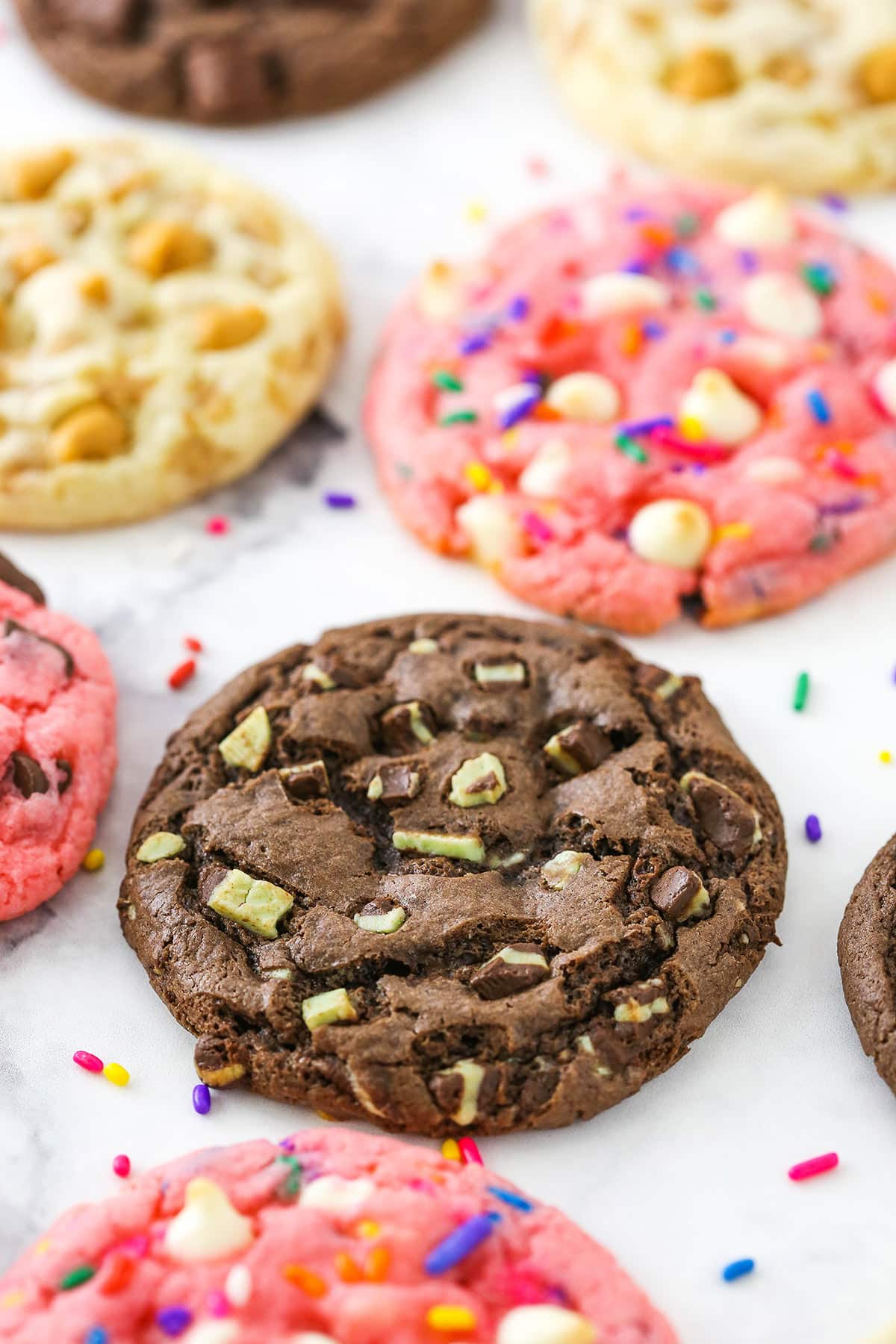 A mint chocolate chip cake mix cookie beside two strawberry Funfetti cake mix cookies and a toffee butterscotch one