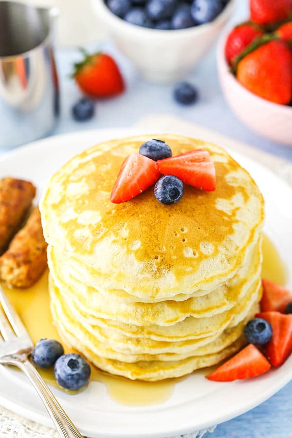Stack of pancakes on a plate with strawberries, blueberries and maple syrup.