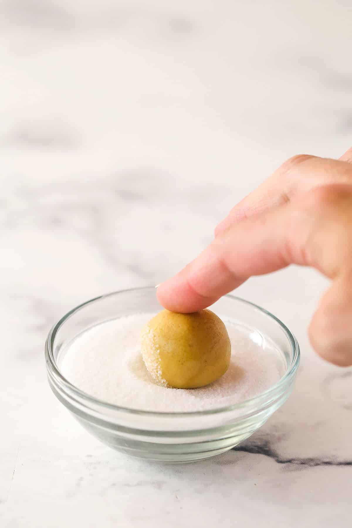 Rolling a cookie dough ball in a small bowl of sugar.