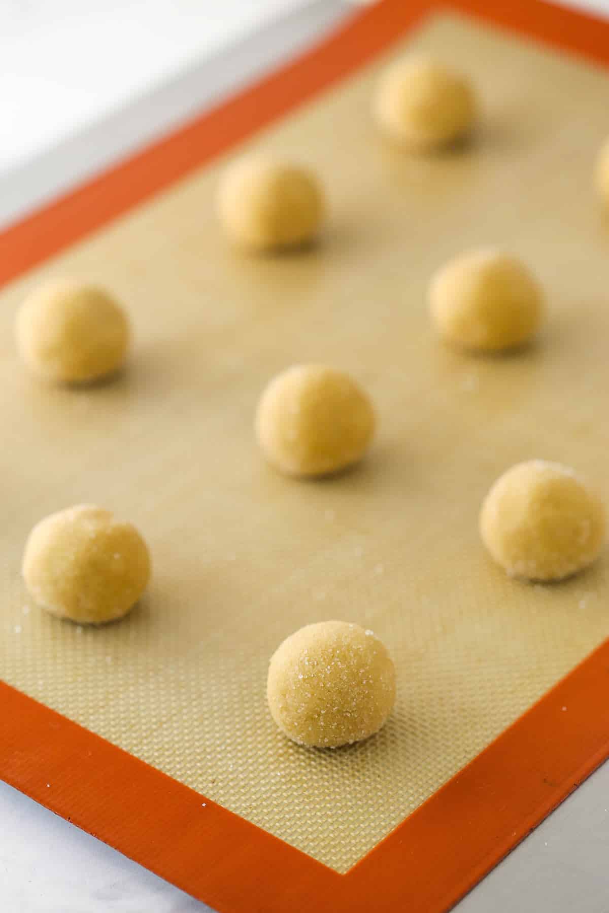 Cookie dough balls on a baking sheet with a silicone baking mat.