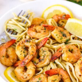Shrimp scampi in a bowl over linguine with fresh lemon wedges garnishing the dish