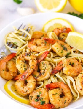 Shrimp scampi in a bowl over linguine with fresh lemon wedges garnishing the dish