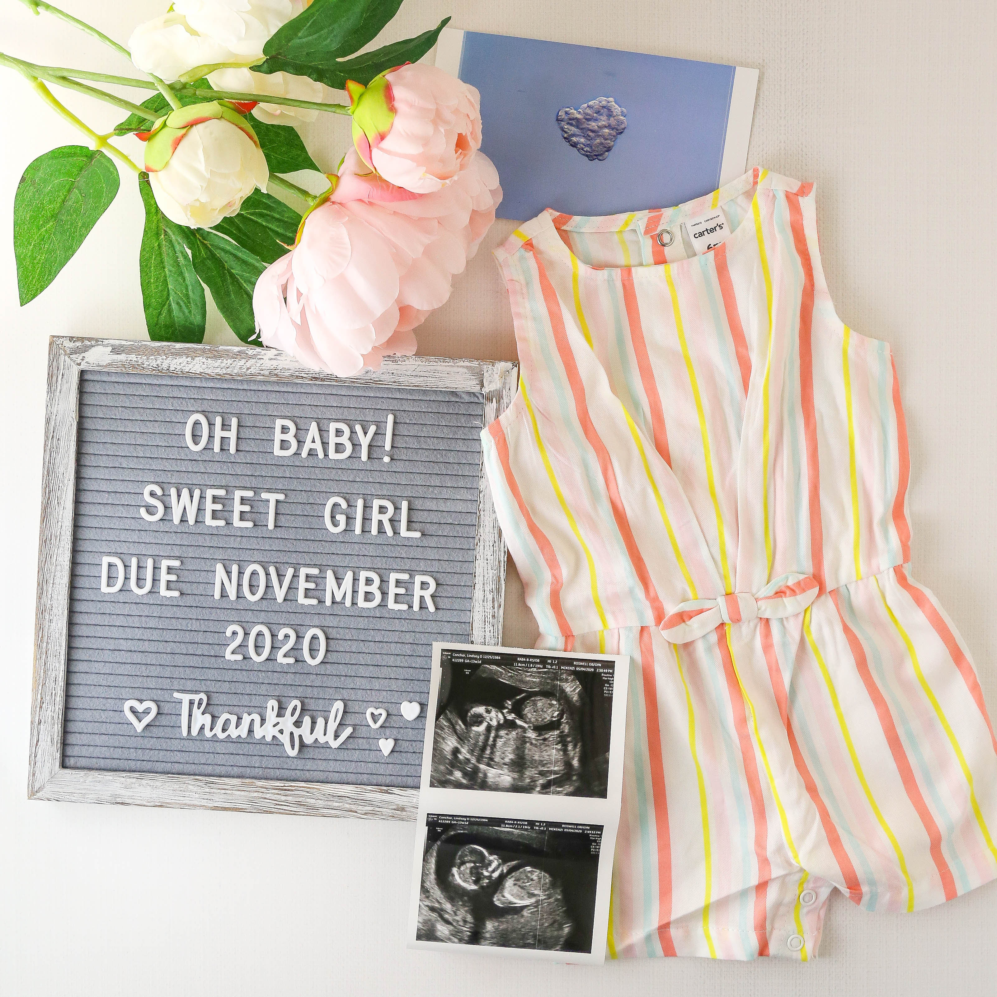 baby announcement photo with some flowers, sonogram photo, baby outfit and letterboard that says "oh baby! sweet girl due november 2020"