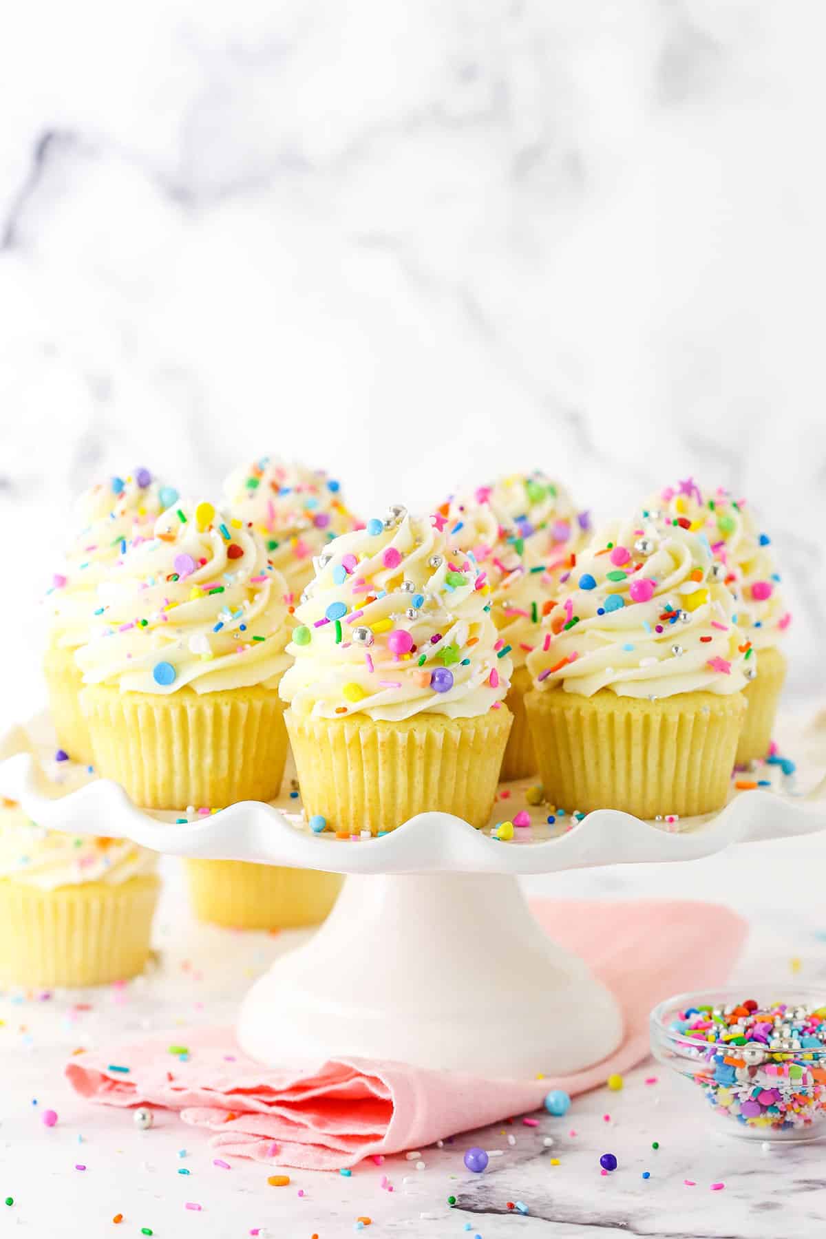 Homemade vanilla cupcakes with sprinkles on a white stand