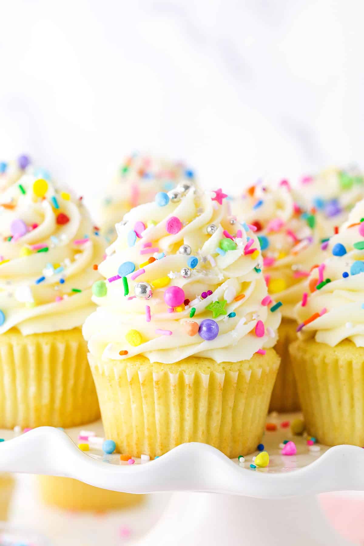 Close up of vanilla cupcakes with vanilla frosting and rainbow sprinkles