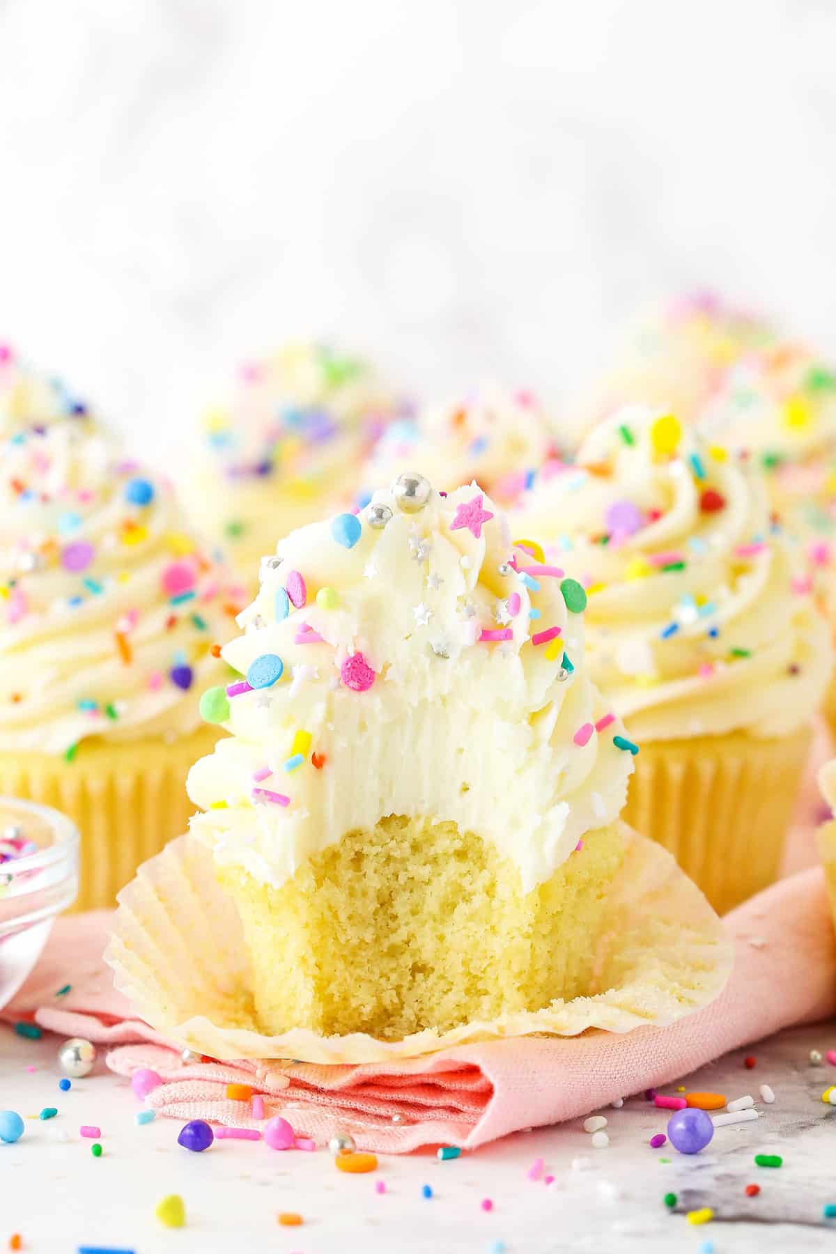 Vanilla cupcake with frosting and sprinkles with a bite taken out of it