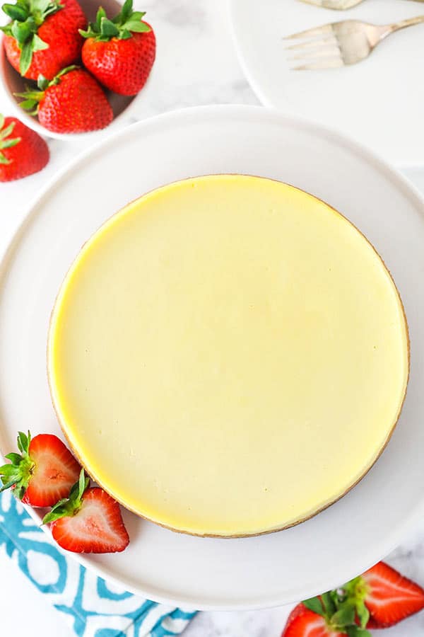 Top view of a cheesecake on a white plate surrounded by strawberries