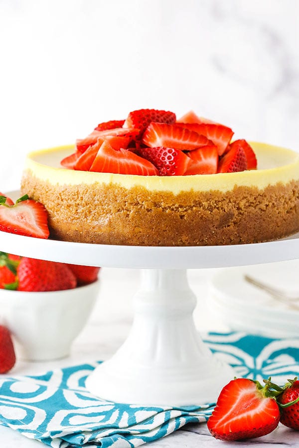 Side view of an instant pot cheesecake on a stand topped with sliced strawberries.