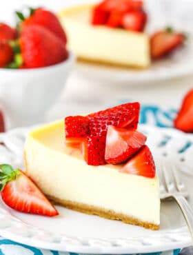 Side view showing a slice of cheesecake on a white plate topped with strawberries.