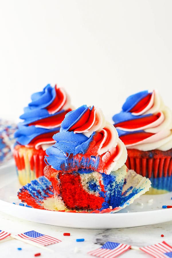 red, white and blue cupcakes on white plate, one with a bite taken out