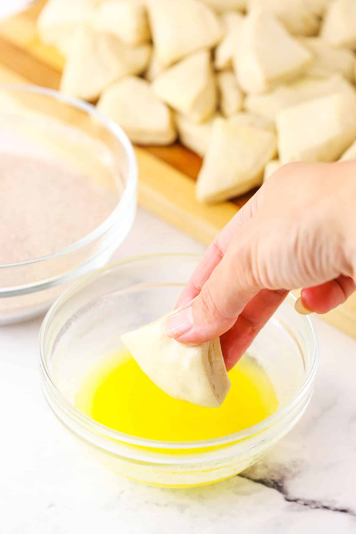 Step in making Apple Fritter Monkey Bread showing cut biscuit pieces being dipped into butter