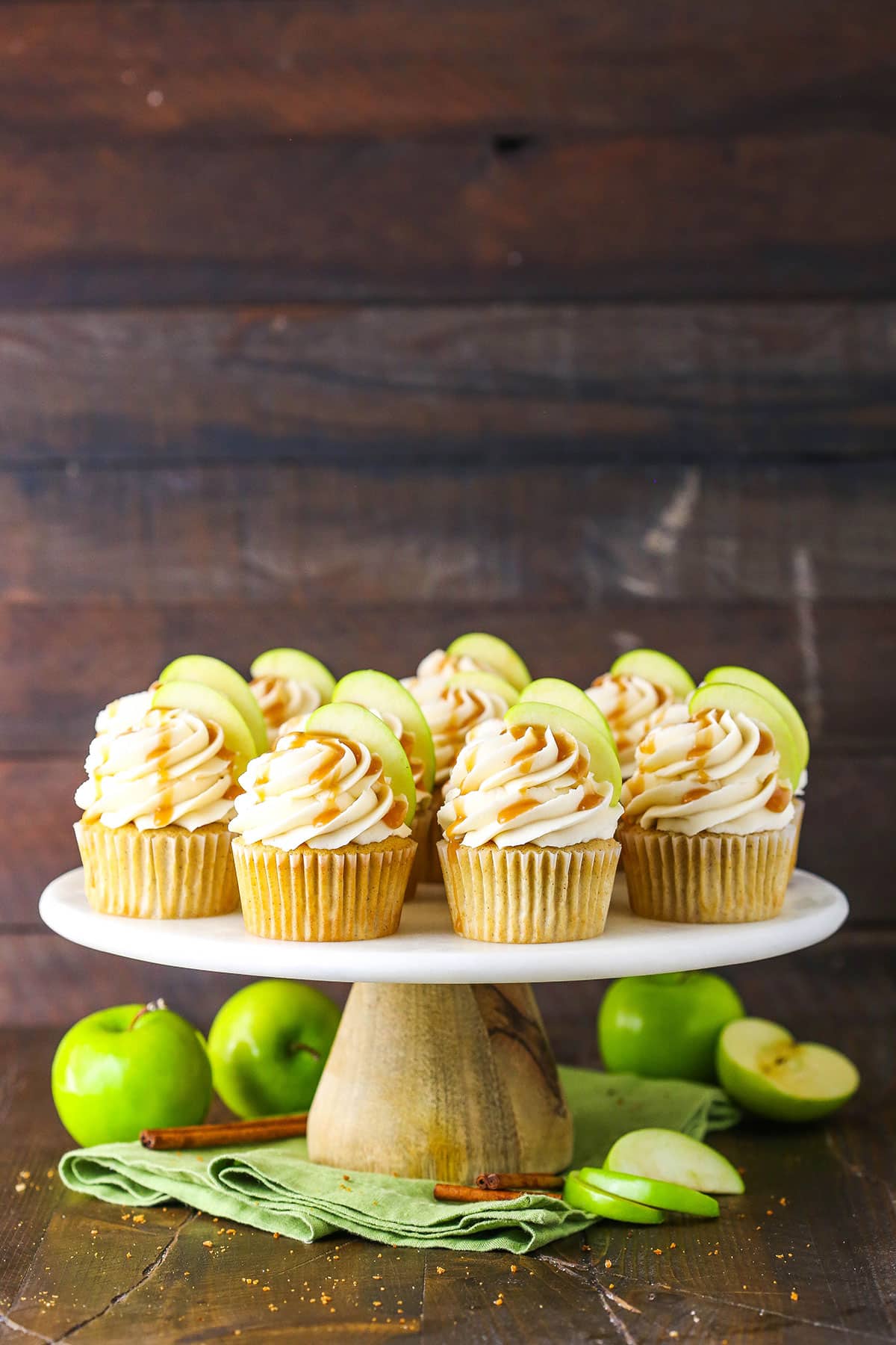 Caramel Apple Cupcakes topped with frosting swirls, a slice of apple and caramel sauce on a cake stand