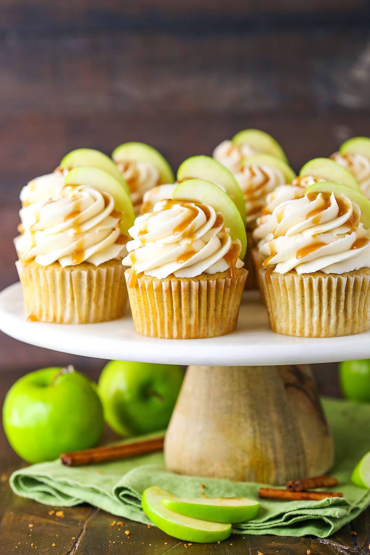 Caramel Apple Cupcakes topped with frosting swirls, a slice of apple and caramel sauce on a cake stand