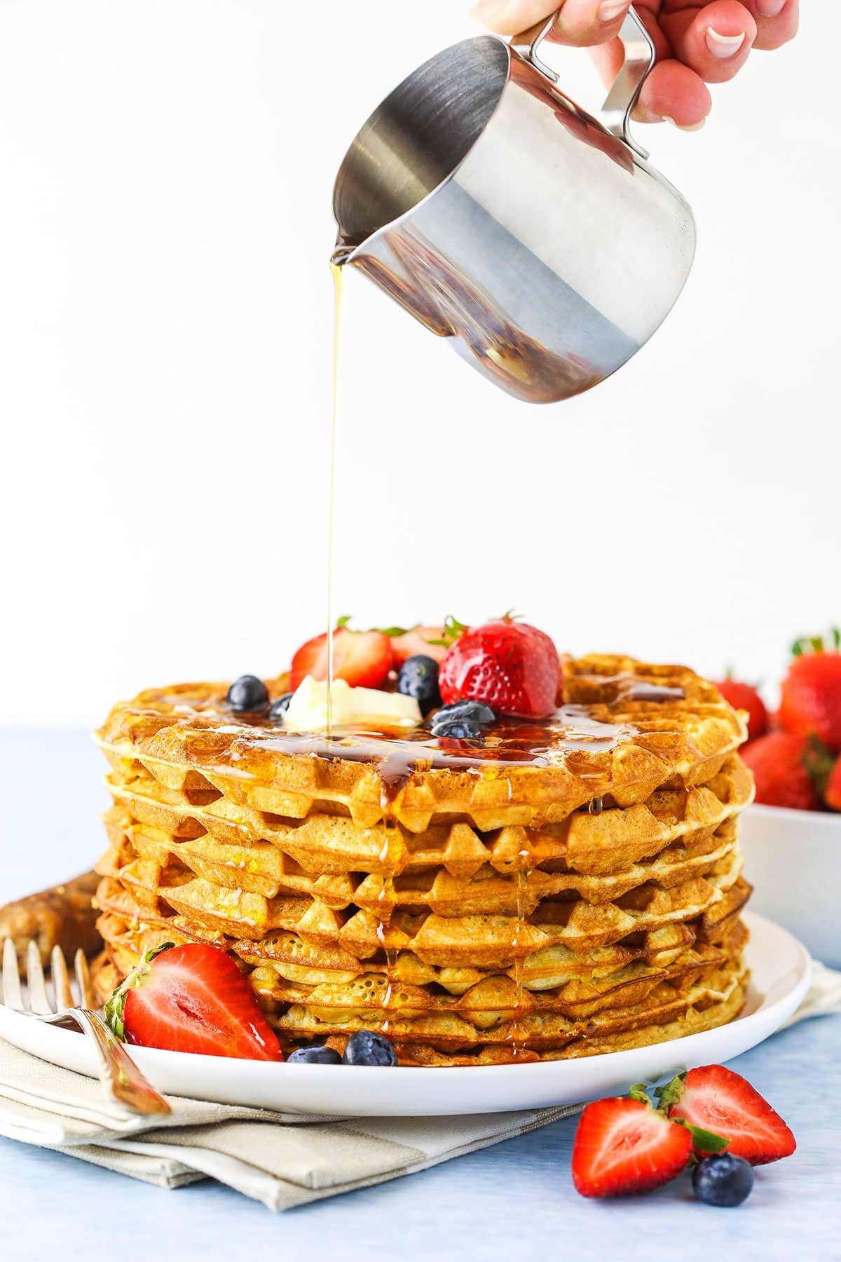 pouring syrup onto stack of waffles