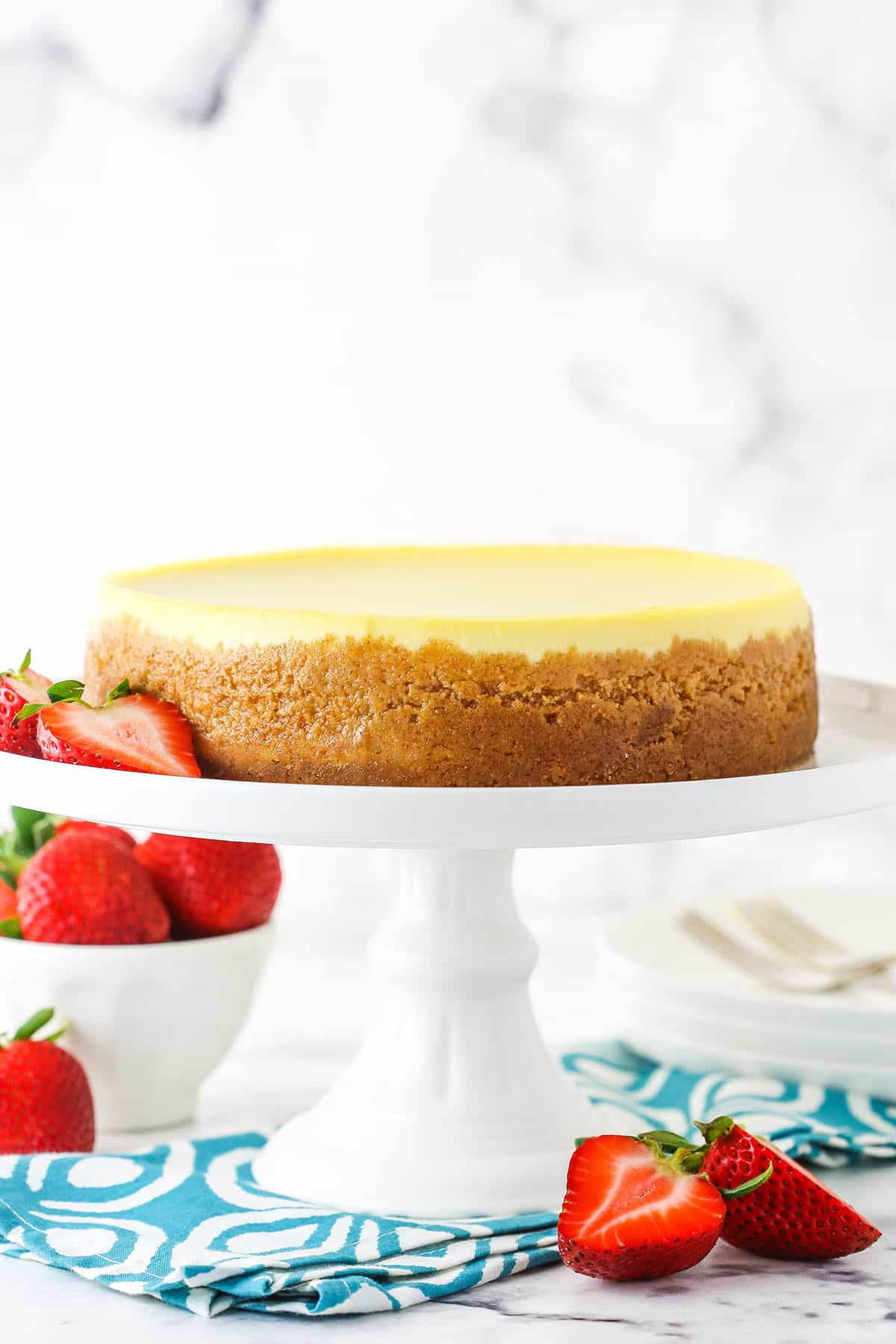 Side view of a full Instant Pot Cheesecake on a white cake stand