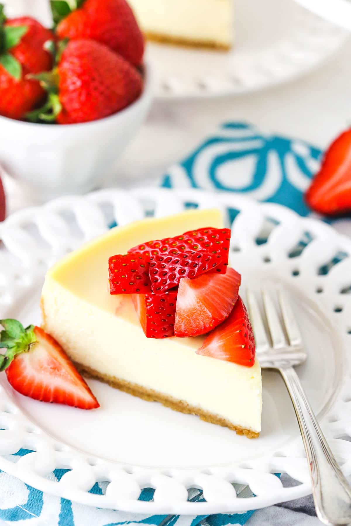 A slice of Instant Pot Cheesecake topped with cut strawberries on a white plate with a fork