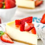 A slice of Instant Pot Cheesecake topped with cut strawberries on a white plate with a fork