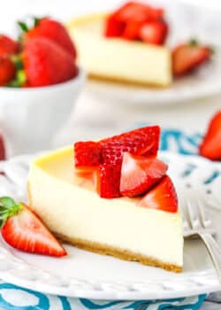 A slice of Instant Pot Cheesecake topped with cut strawberries on a white plate with a fork