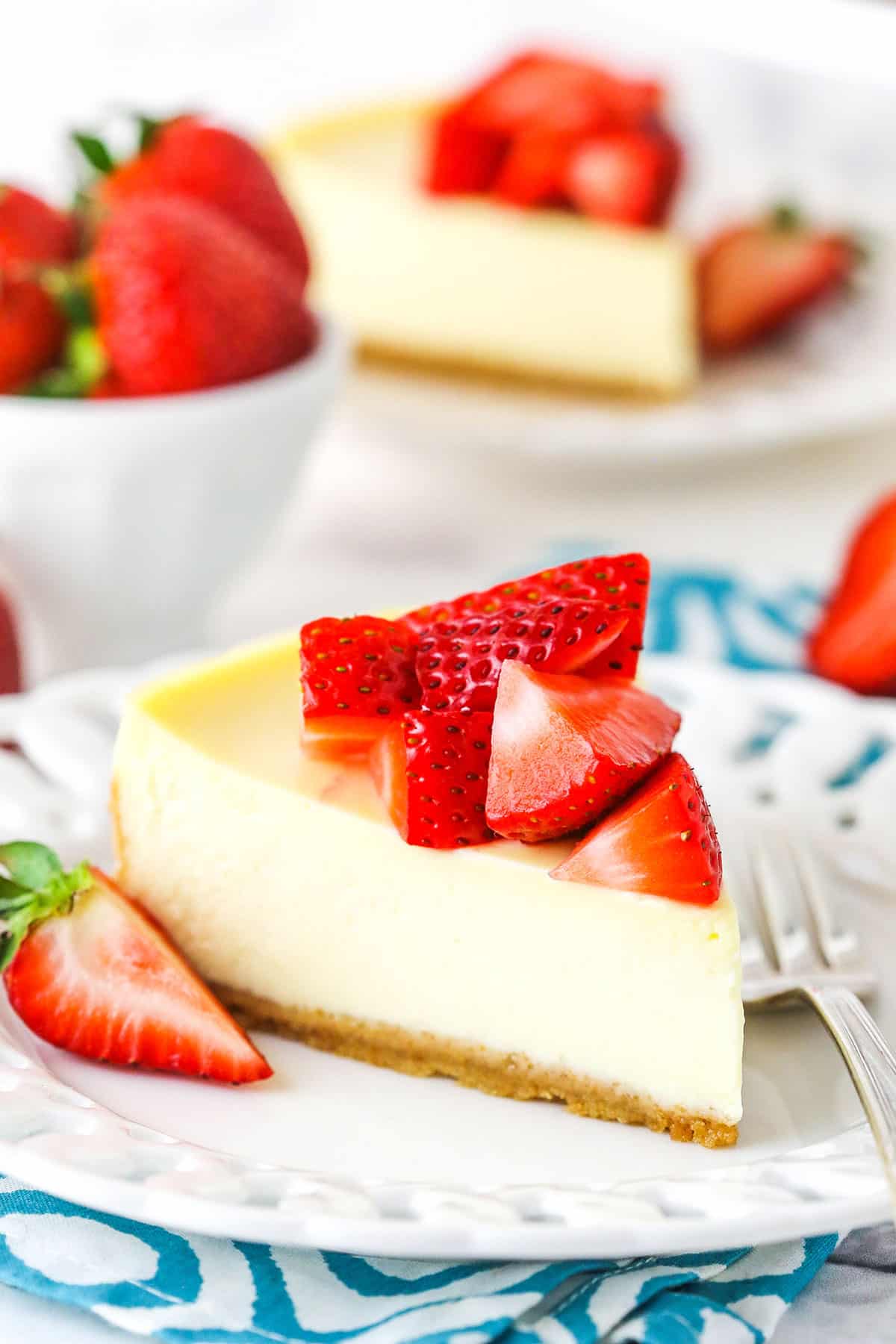 A slice of Instant Pot Cheesecake topped with cut strawberries on a white plate with a fork