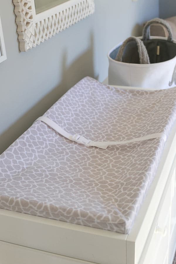 A White Changing Table with a Giraffe Patterned Changing Pad on Top