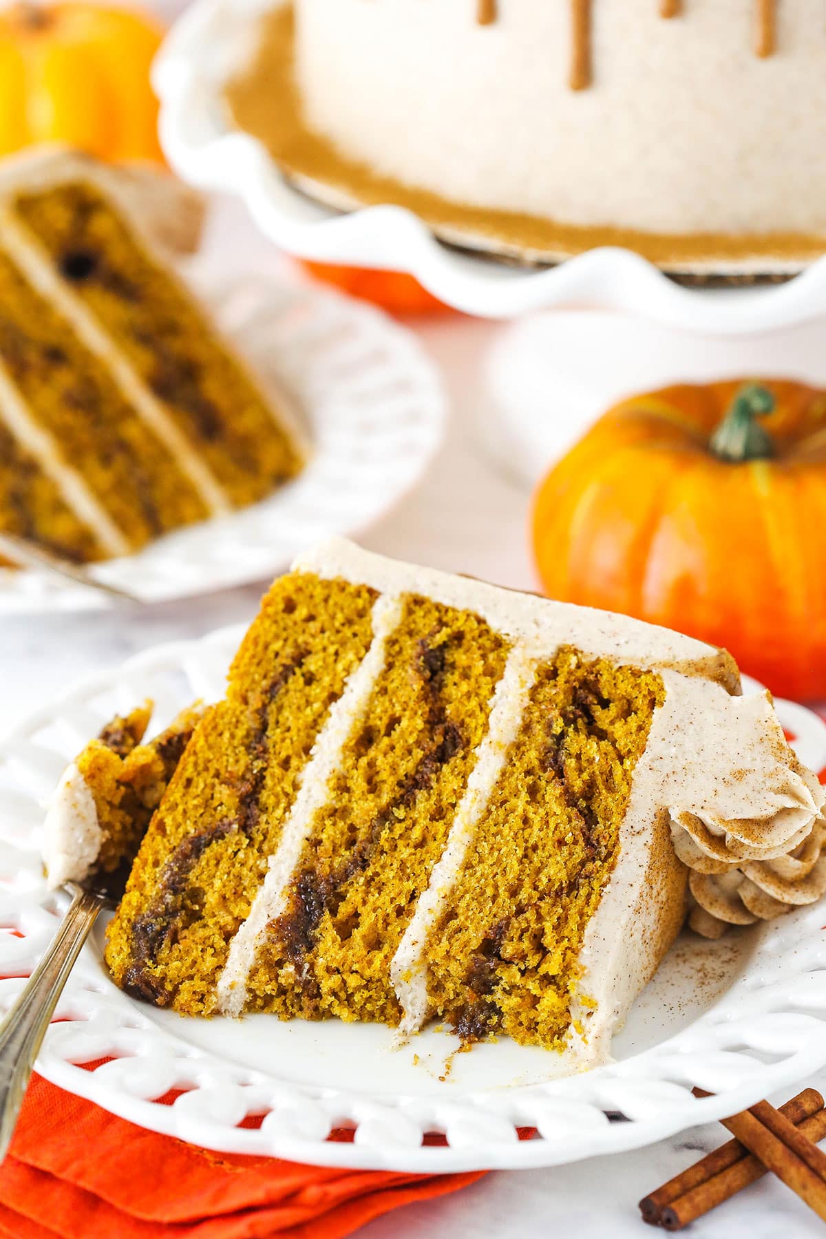 A slice of Cinnamon Sugar Swirl Pumpkin Layer Cake on it's side on a white plate with a bite taken.