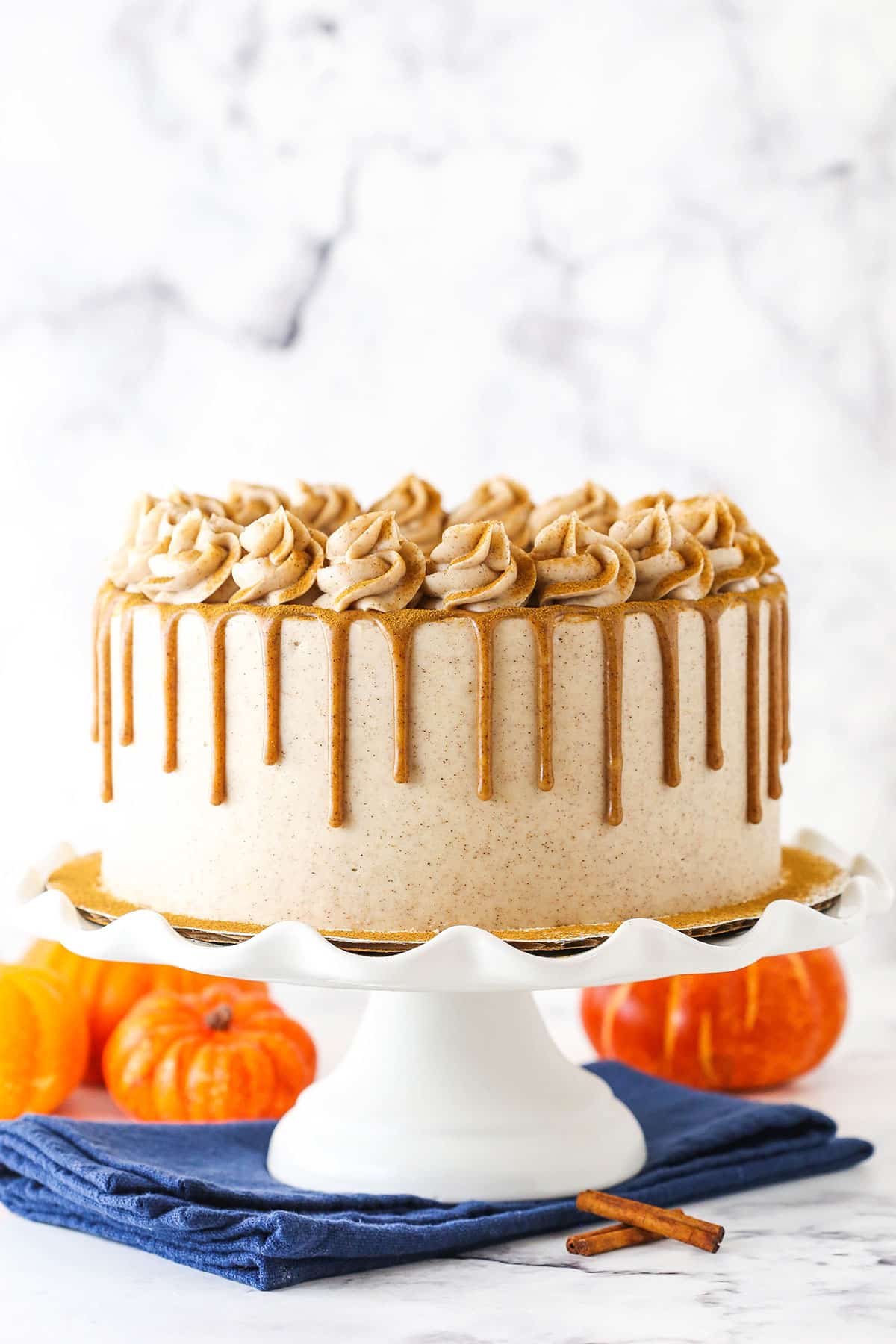 Cinnamon Sugar Swirl Pumpkin Layer Cake with frosting swirls and caramel drip on a white cake stand.