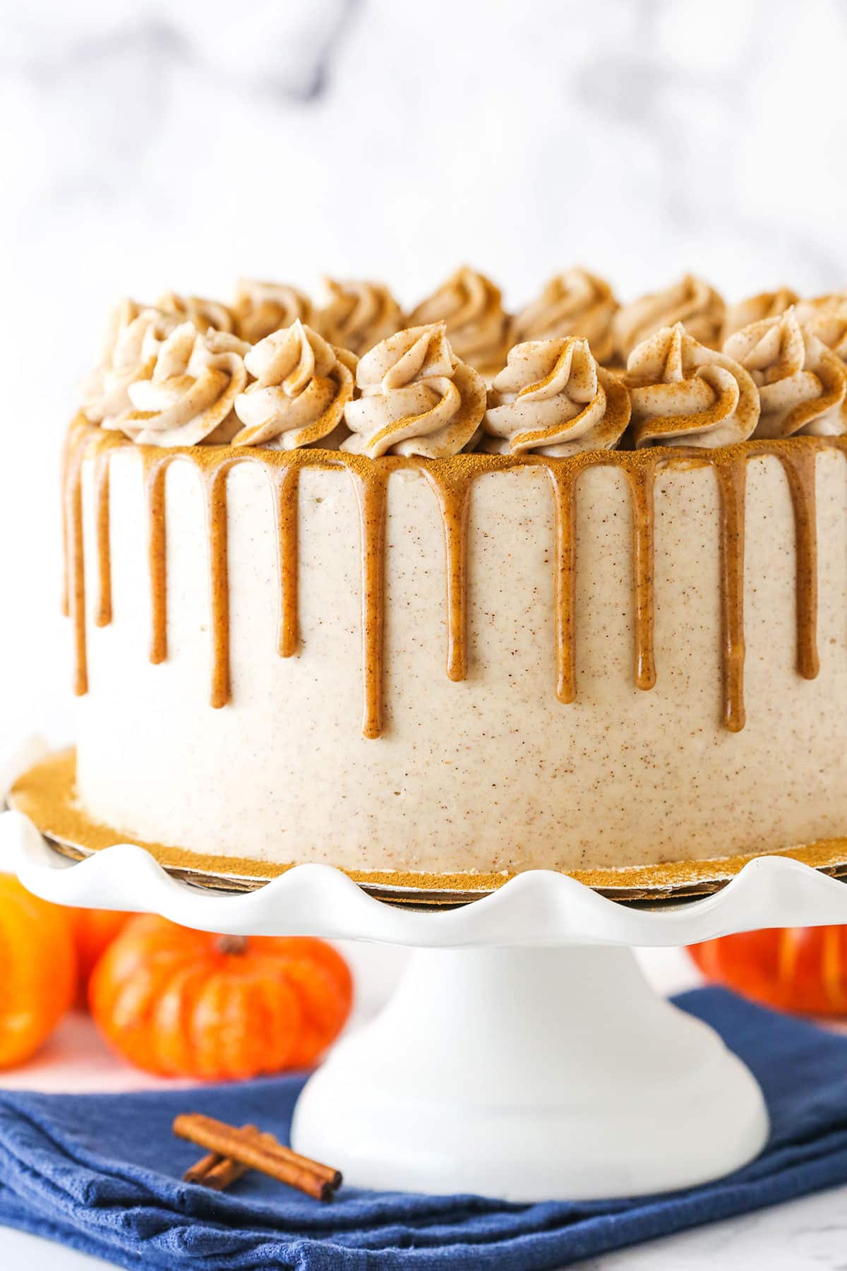 Cinnamon Sugar Swirl Pumpkin Layer Cake with frosting swirls and caramel drip on a white cake stand.