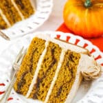 A slice of Cinnamon Sugar Swirl Pumpkin Layer Cake on it's side on a white plate with a fork.