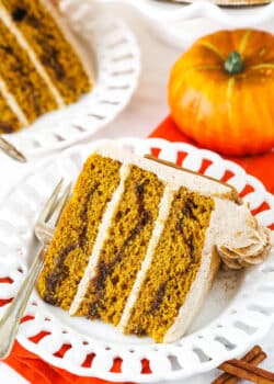 A slice of Cinnamon Sugar Swirl Pumpkin Layer Cake on it's side on a white plate with a fork.