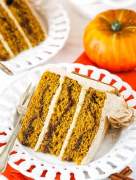 A slice of Cinnamon Sugar Swirl Pumpkin Layer Cake on it's side on a white plate with a fork.