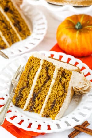 A slice of Cinnamon Sugar Swirl Pumpkin Layer Cake on it's side on a white plate with a fork.