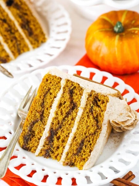 A slice of Cinnamon Sugar Swirl Pumpkin Layer Cake on it's side on a white plate with a fork.