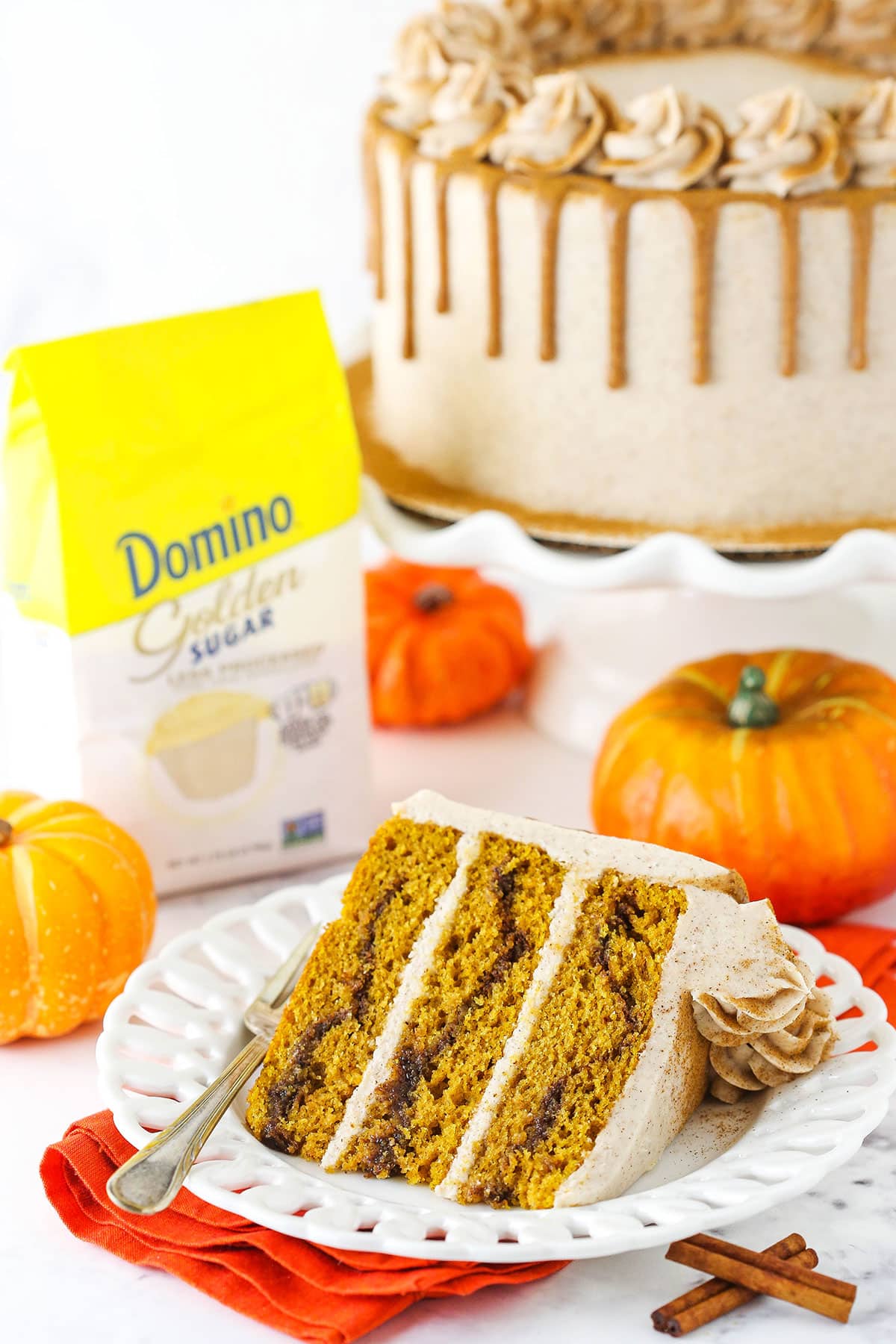 A slice of Cinnamon Sugar Swirl Pumpkin Layer Cake with cake and Domino golden sugar in the background