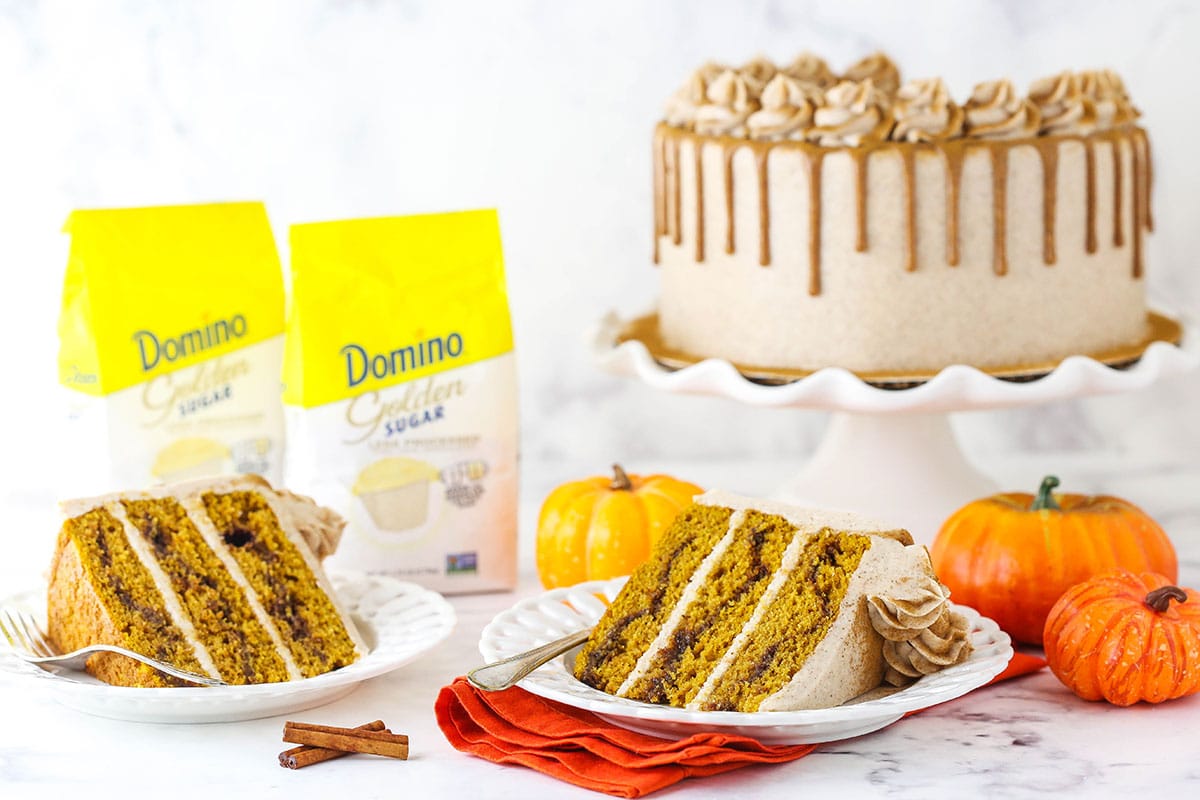 A slice of Cinnamon Sugar Swirl Pumpkin Layer Cake with cake and Domino golden sugar in background