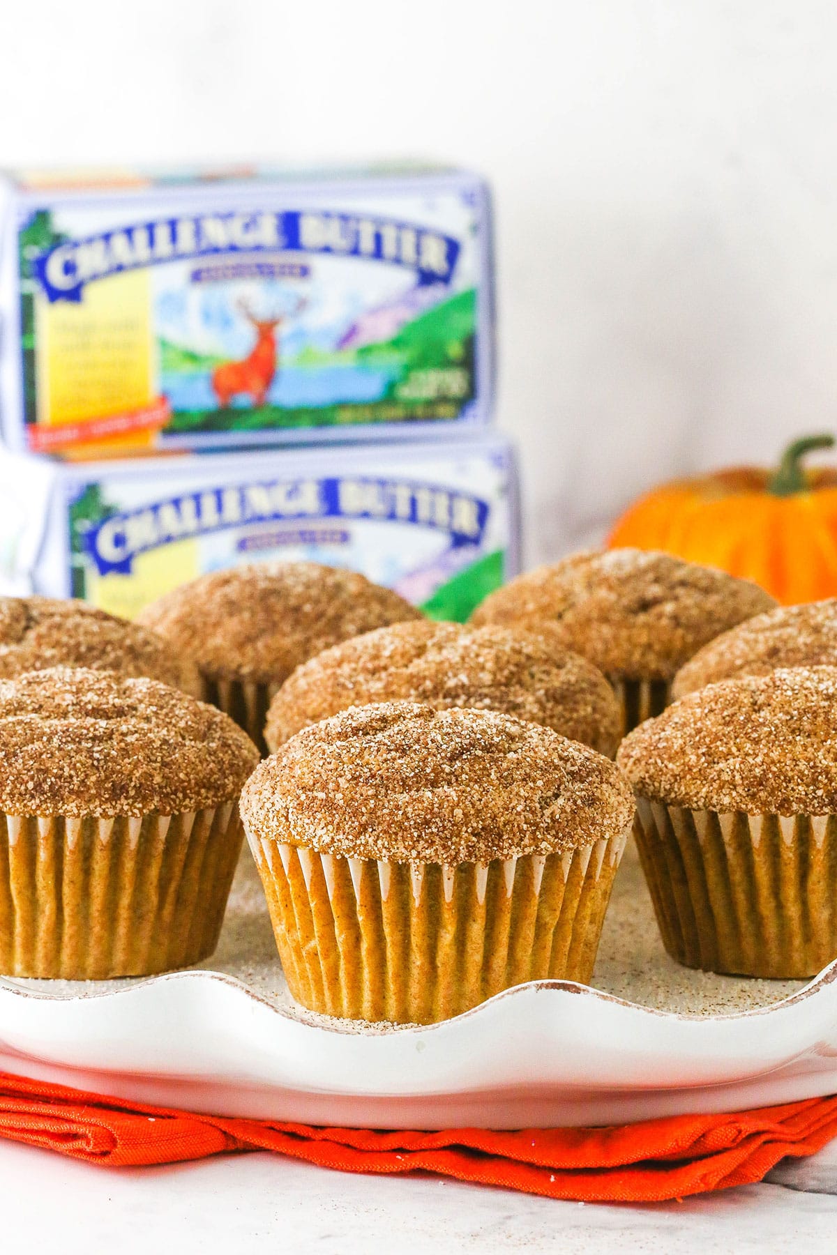 cinnamon sugar pumpkin muffins on white plate with challenge butter in background