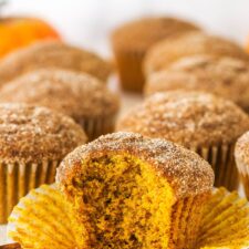 A pumpkin muffin with bite missing, with more muffins in the background.
