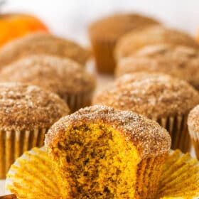 A pumpkin muffin with bite missing, with more muffins in the background.