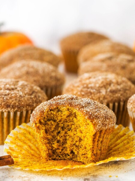 A pumpkin muffin with bite missing, with more muffins in the background.