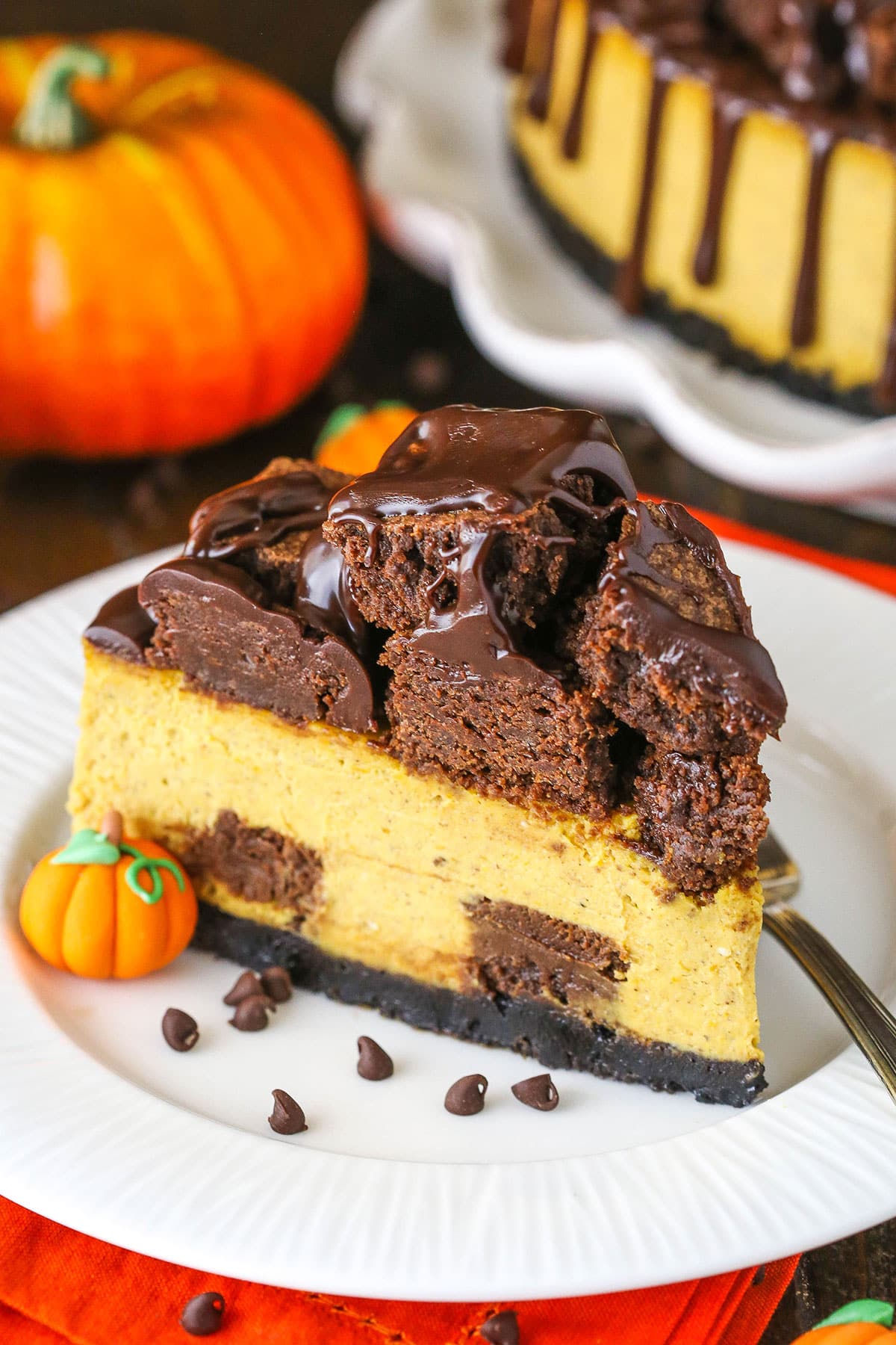 A slice of Copycat Chunkin Chocolate Pumpkin Cheesecake topped with brownie cubes and decorated with a candy pumpkin