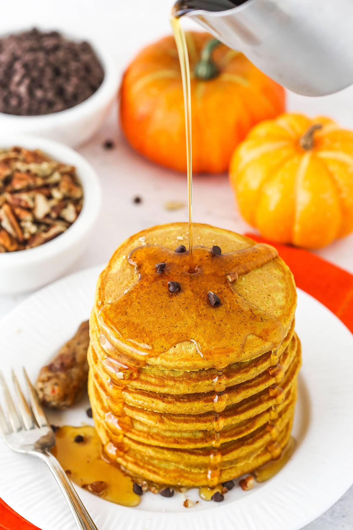 Pouring maple syrup over a pile of pancakes.