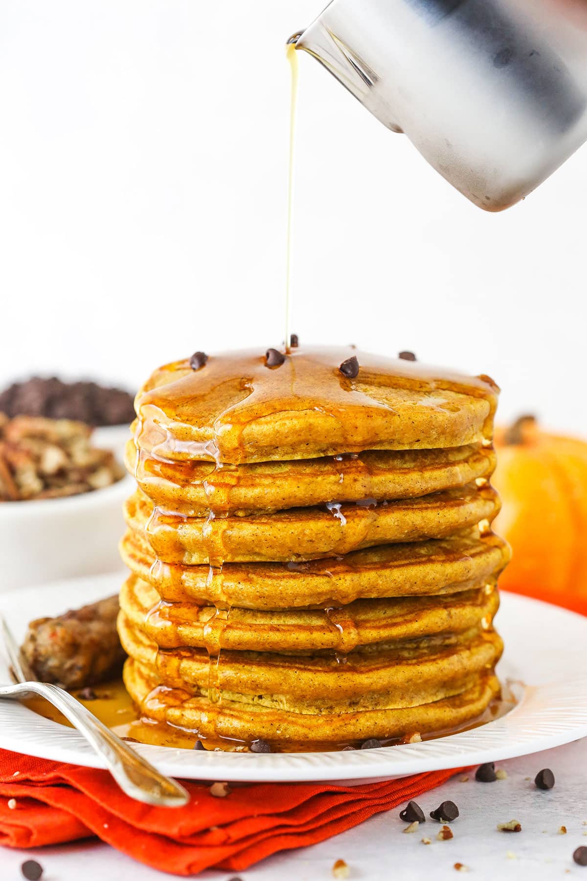 Pouring maple syrup over a pile of pumpkin pancakes.