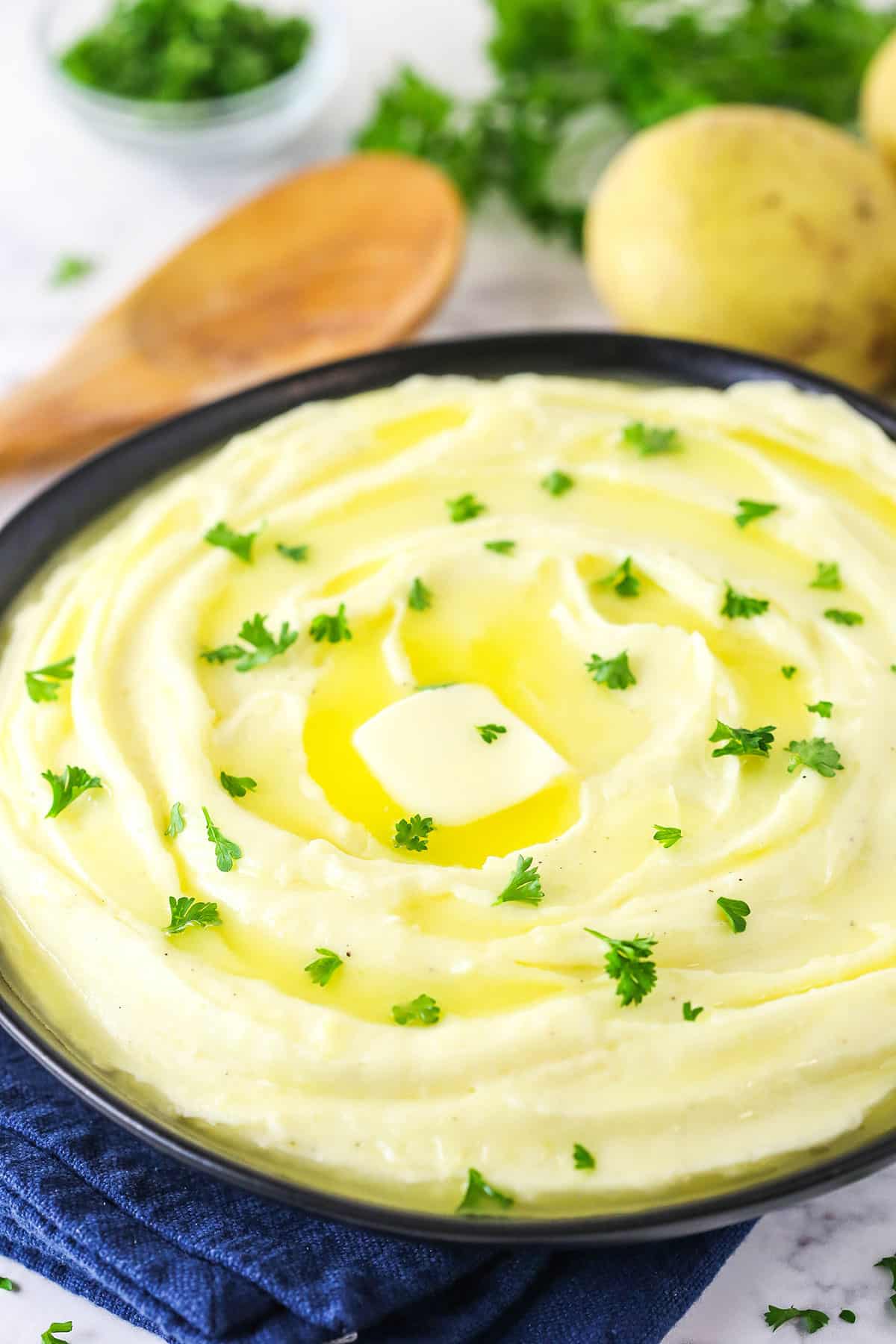 This silky and creamy mashed potatoes recipe with heavy cream and butter is the perfect veggie side for your favorite dinners. A bowl of creamy mashed potatoes with a knob of butter and fresh parsley on top.