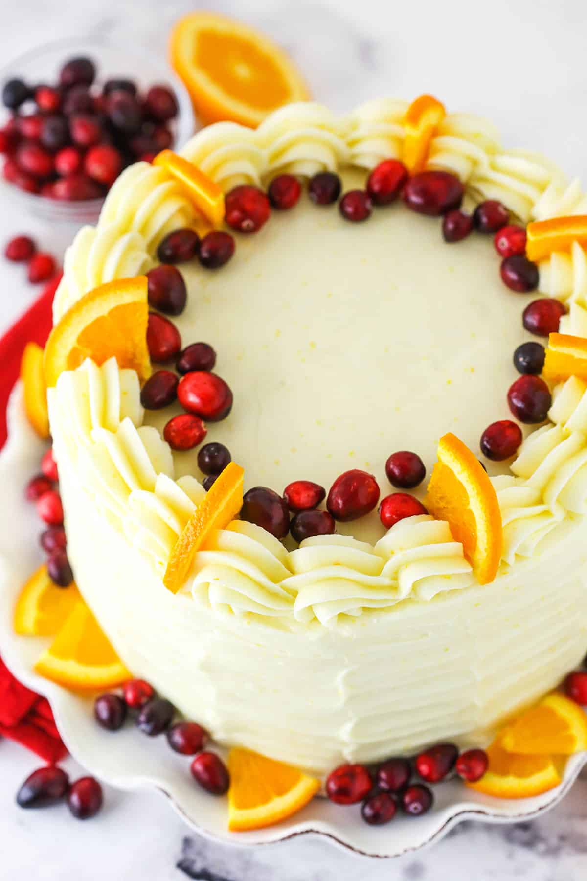 Overhead view of a Cranberry Orange Layer Cake topped with cranberries, orange slices and white swirls.