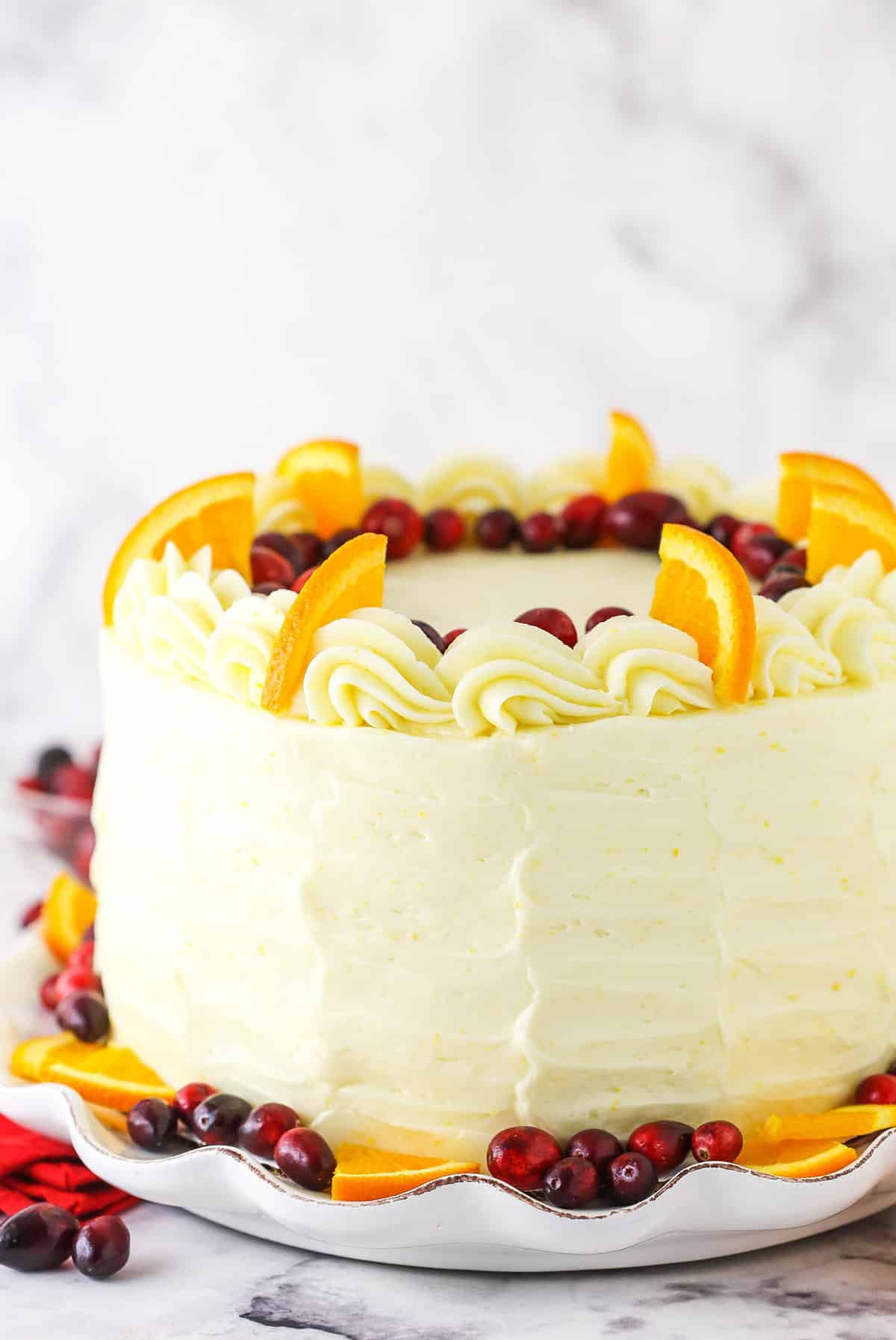 Side view of a Cranberry Orange Layer Cake topped with cranberries, orange slices and white swirls.