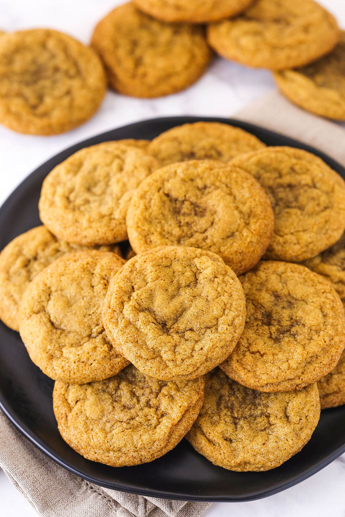 A plate full of molasses cookies with five stray cookies on the counter.