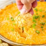 A chip scooping up some Cheesy Buffalo Dip from a clear bowl.