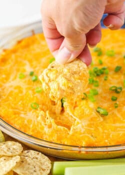 A chip scooping up some Cheesy Buffalo Dip from a clear bowl.